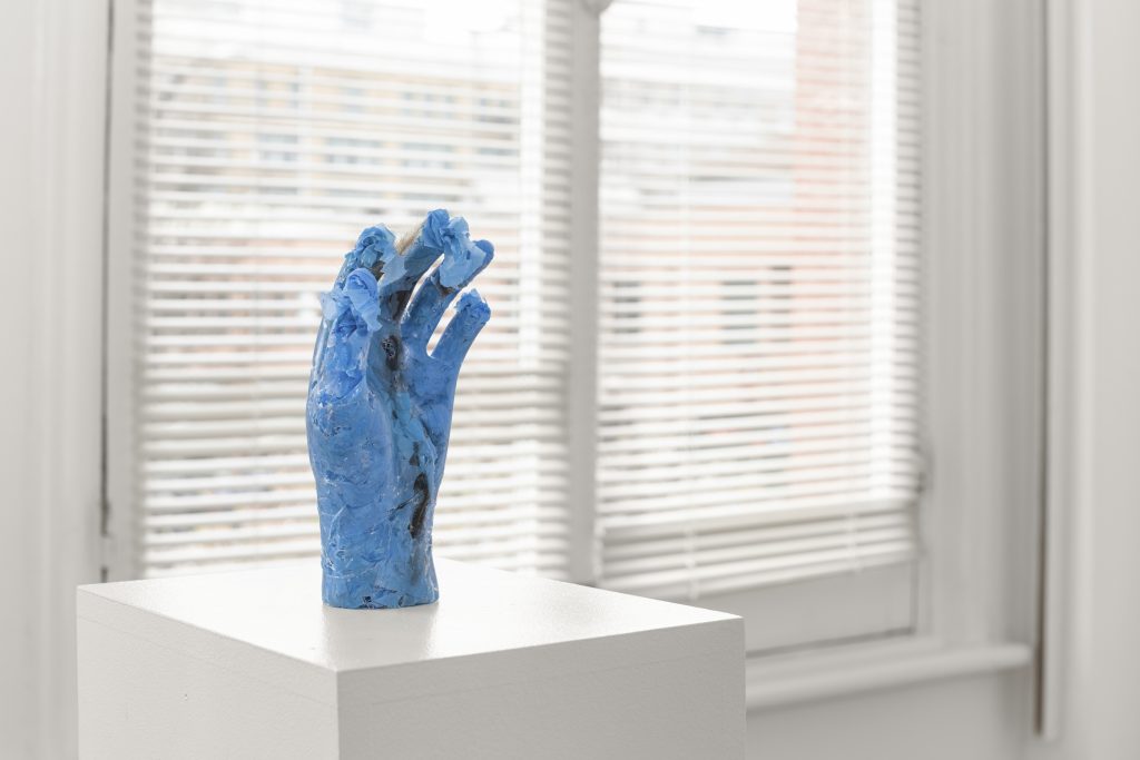 Carollyne Yardley, Becoming Plastic, from the Becoming Plastic series, 2022. Gifted human hair, used blue nitrile gloves, resin, 7.5” x 2.5” x 2.5”. Installation view from Becoming Plastic at Deluge Contemporary Art, 2022. Photograph by Spartan Media.